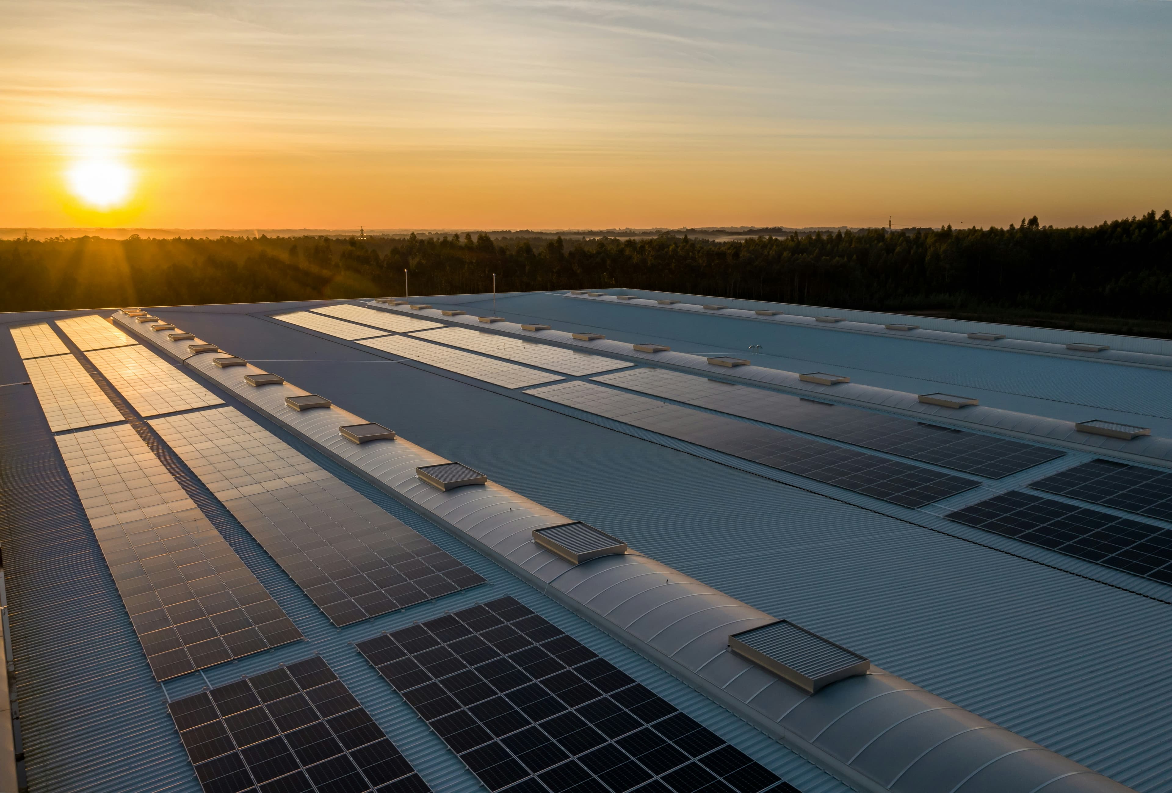 Aerial view of solar panels on a large roof in a rural area at sunset.